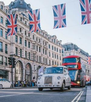 White taxi car with a red bus in the background and British flags in the foreground