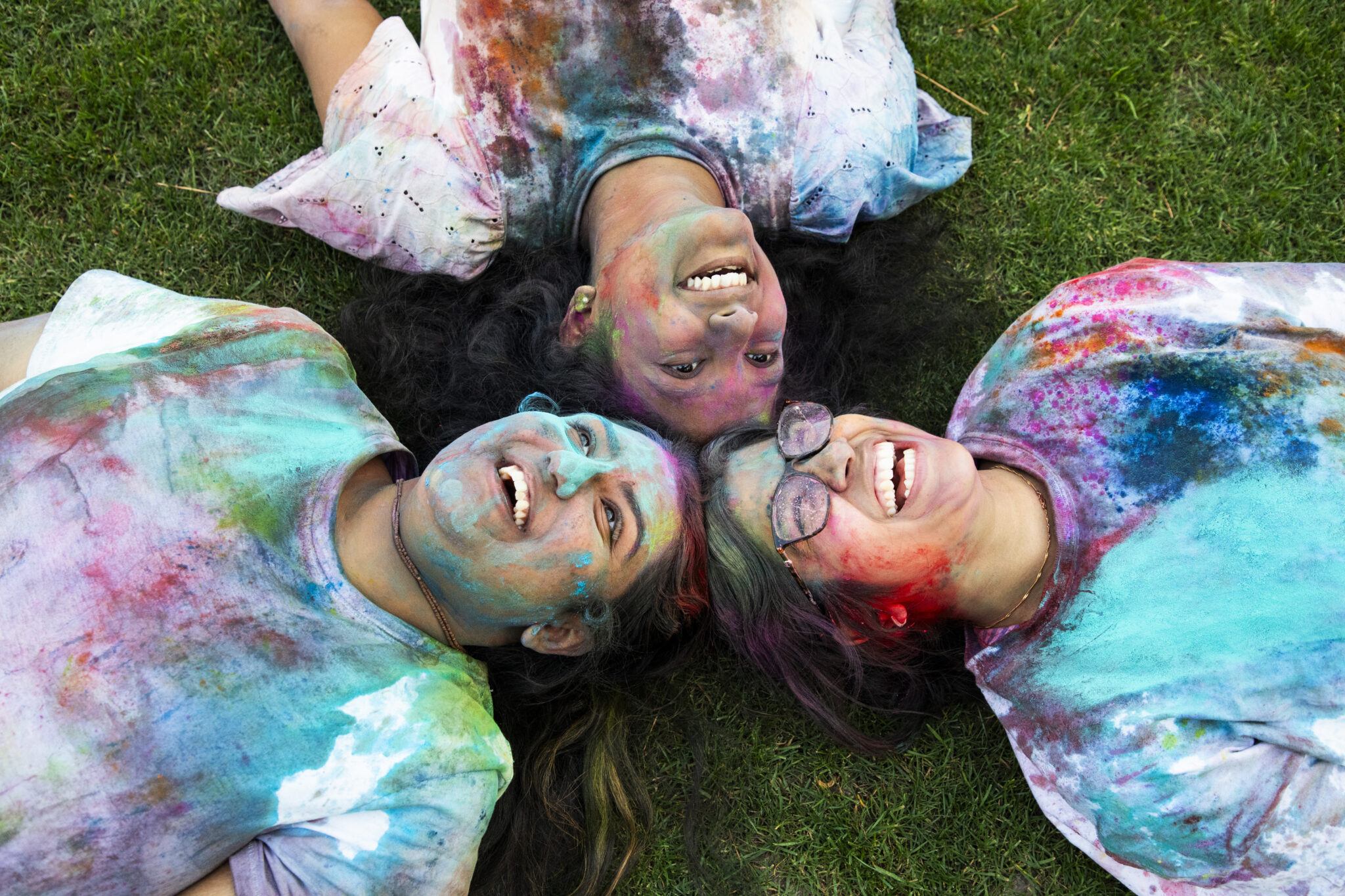 Students on the ground smiling covered in Holi colors