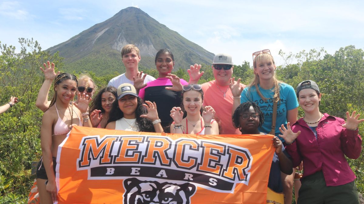 a 2025 Spring Break study abroad group posing with a Mercer flag at Arenal National Park & Volcano in Costa Rica